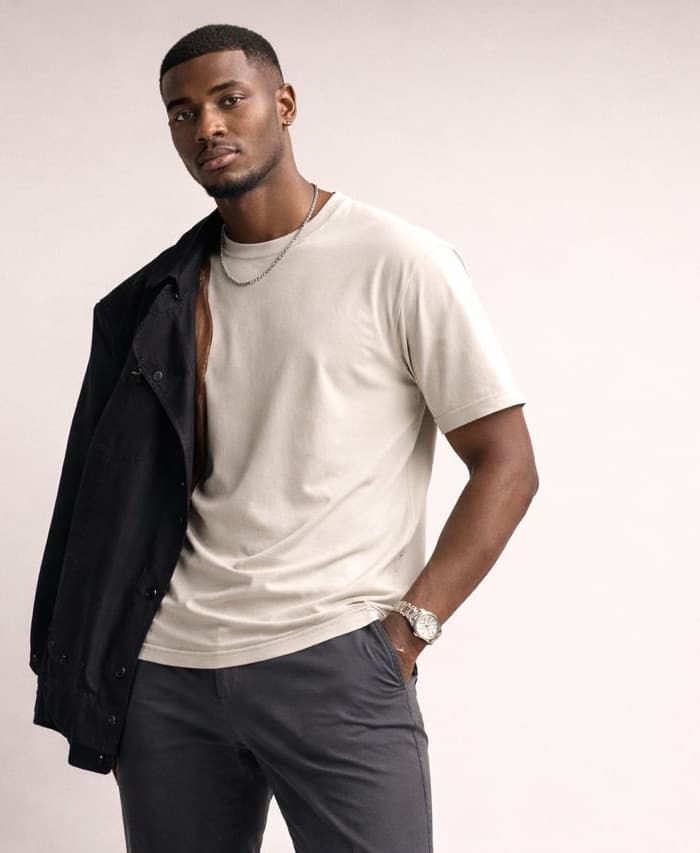 Model in a cream KODtrends tee and charcoal trousers, holding a black jacket